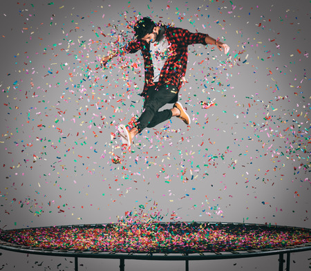 Carefree fun. Mid-air shot of handsome young man jumping on trampoline with confetti all around himの写真素材