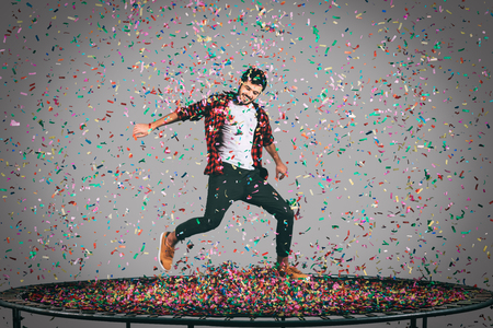 Trampoline and confetti. Mid-air shot of handsome young man jumping on trampoline with confetti all around himの写真素材