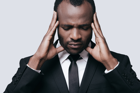 Feeling upset. Young African man in formalwear touching his head with hands while standing against grey backgroundの写真素材