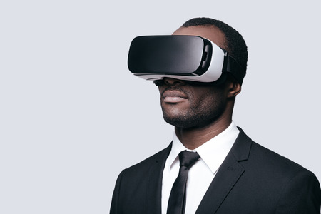 Another reality is here! Handsome young African man in VR headset standing against grey backgroundの写真素材