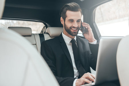 Focusing on work. Handsome young businessman working on his laptop and talking on the phone while...