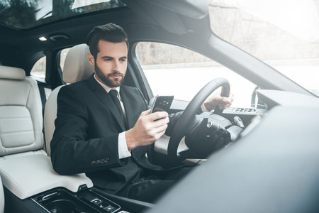 Always available. Handsome young businessman looking on his smart phone while sitting on the front...