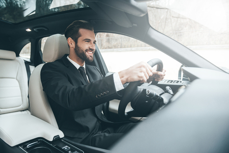 On the way to success. Confident young businessman sitting on the front seat and smiling while driving a carの写真素材