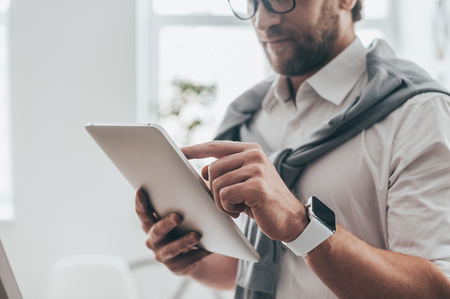 Using modern technologies. Close-up of young businessman working on digital tablet while standing in creative office の写真素材