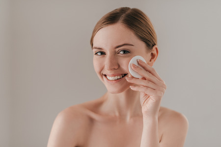 Time for skin care. Studio portrait of attractive woman cleansing her skin with a cotton pad while standing against backgroundの写真素材