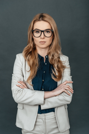 Beautiful and successful. Young attractive woman in smart casual wear keeping arms crossed and looking at camera while standing against grey backgroundの写真素材