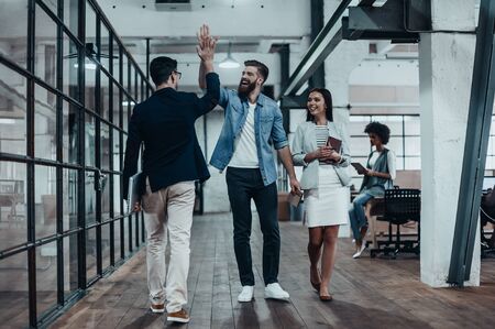 High-five!  Full length of two cheerful young business people giving high-five while their colleague looking at them and smilingの写真素材