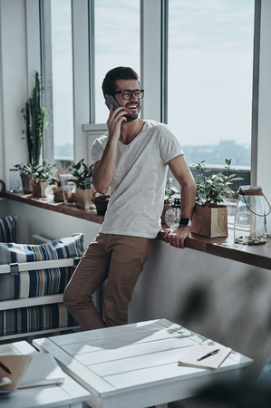 Receiving good feedbacks. Handsome young man talking on his smart phone while leaning on the window sillの写真素材