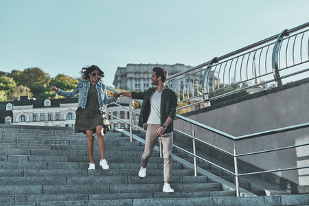 Happy to be together. Full length of handsome man and young attractive woman holding hands while walking down the stairs outdoorsの写真素材
