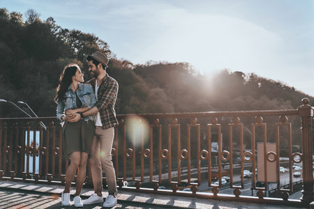 Great date. Full length of beautiful young couple embracing and looking at each other while standing on the bridge outdoorsの写真素材