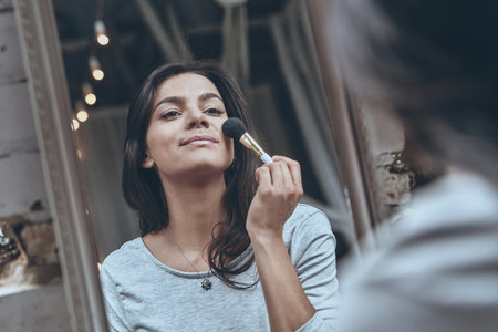 Last details.  Reflection of attractive young woman putting on some make-up while spending time at...