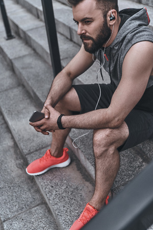 Music in his heart. Handsome young man in sport clothing listening music while sitting on the steps outsideの写真素材