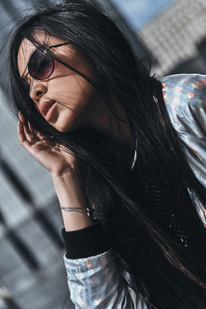 Looking amazing. Beautiful young woman in casual wear keeping hand in hair while spending time outdoorsの写真素材
