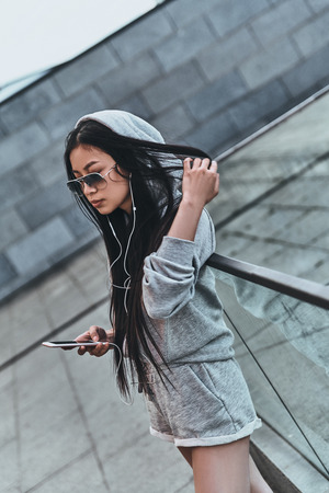 Feeling the beat. Beautiful young woman in casual wear holding a smart phone while standing outdoorsの写真素材