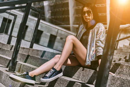 Enjoying nice day. Beautiful young Asian woman in casual wear looking at camera while sitting on the...