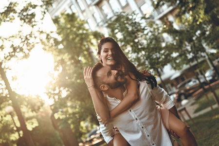 Totally in love. Handsome young man giving his girlfriend a piggyback ride while spending time togetherの写真素材