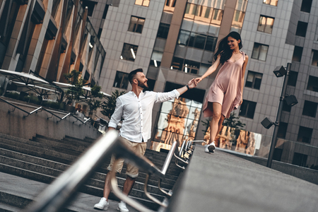 Just having fun. Full length of playful young couple holding hands and smiling while walking down the stairs outdoorsの写真素材