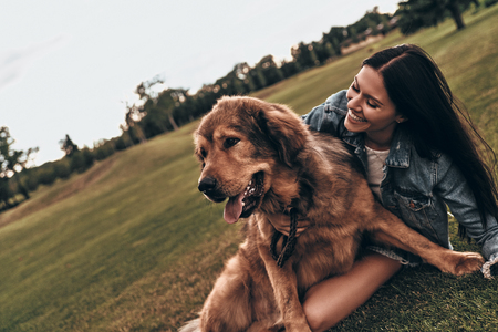 Moments of joy. Beautiful young woman keeping eyes closed and smiling while playing with her dog outdoorsの写真素材