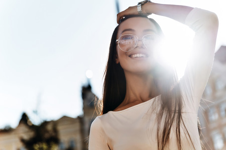 Feeling so happy! Attractive young woman keeping hand in hair and smiling while standing outdoorsの写真素材
