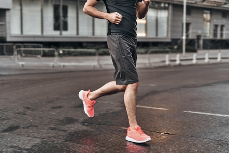 Running is a great cardio. Close up of man in sport clothing running along the city streetの写真素材