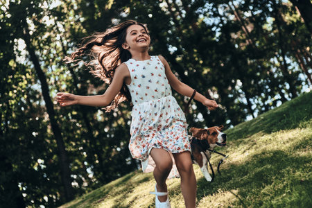 Feeling free and happy. Cute little girl smiling while running with her dog outdoorsの写真素材