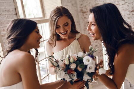 Attractive young bride holding a wedding bouquet and smiling while talking to her charming bridesmaidsの写真素材
