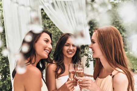 Attractive young bride toasting with champagne with her beautiful bridesmaids while standing outdoors togetherの写真素材