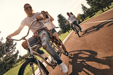 Enjoying every minute together. Group of happy young people in casual wear smiling while cycling together outdoorsの写真素材