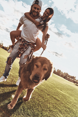 Where are you taking us? Full length of handsome young man carrying young attractive woman on shoulders while walking with their dog outdoorsの写真素材