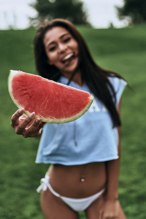 You should try it!  Attractive young woman outstretching hand with a slice of watermelon and smiling while standing outdoorsの写真素材