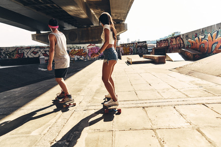 Doing what they love. Full length rear view of modern man and attractive woman skateboarding while hanging out together outdoorsの写真素材