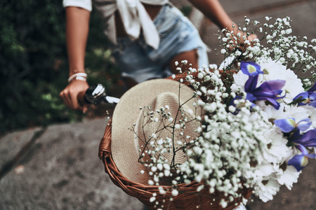Moments of summer. Close-up of young woman riding bicycle with flowers in basketの写真素材