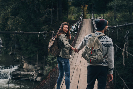 Making each other happy. Young smiling couple holding hands while walking on the suspension bridgeの写真素材