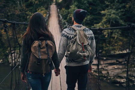 Taking next step. Rear view of young couple stepping on the suspension bridge while hiking together...
