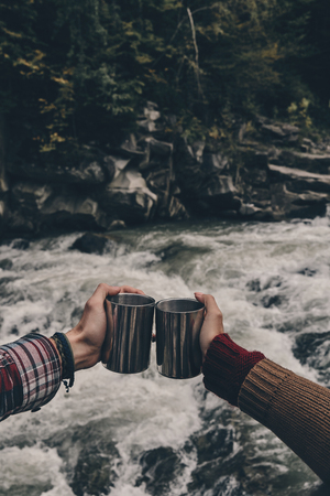 To us! Close up of young couple toasting each other while relaxing on the rocks near the riverの写真素材