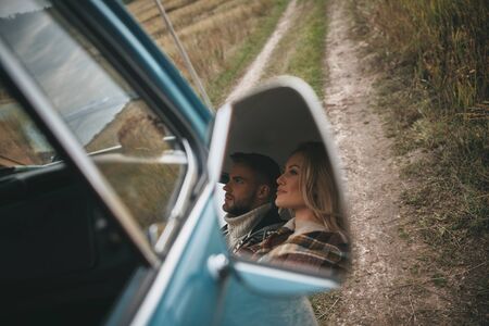 Happy couple traveling. Reflection of beautiful young couple looking away and smiling while sitting in retro style mini vanの写真素材