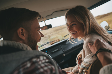 Real love. Happy young couple laughing while sitting on the front passenger seats in retro style mini vanの写真素材