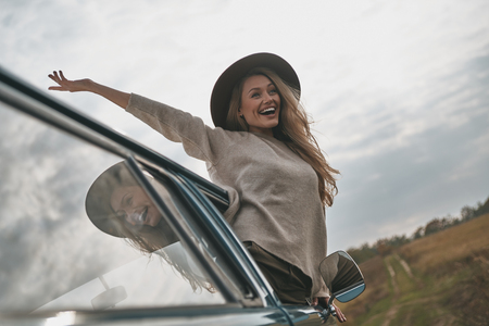 Beautiful day. Attractive young smiling woman leaning out the van?s window and keeping arms outstretched while enjoying the car travelの写真素材