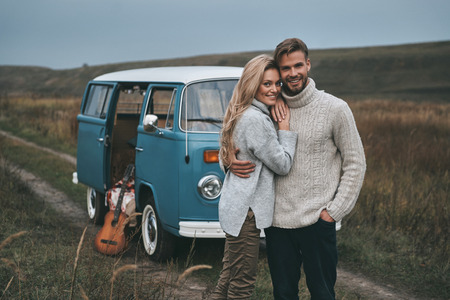 Happy to be together.  Beautiful young couple embracing and smiling while standing near the blue retro style mini vanの写真素材