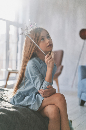 Cute little girl playing with a magic wand while spending time at homeの写真素材