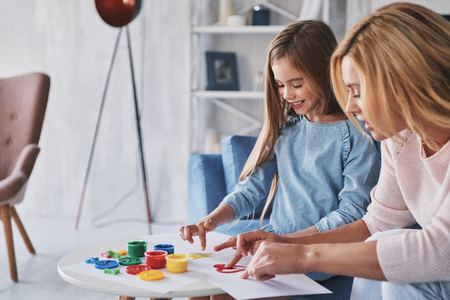 Enjoying drawing together. Mother and daughter painting with fingers and smiling while spending time at homeの写真素材
