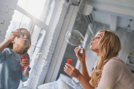 Mother and daughter blowing soap bubbles while spending time at homeの写真素材