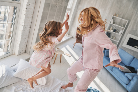 Having fun! Top view of cute little girl jumping on the bed with her mother while spending time at homeの写真素材