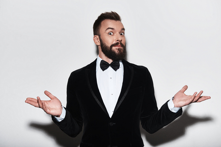 Who knows? Handsome young man in full suit shrugging his shoulders while standing against grey backgroundの写真素材