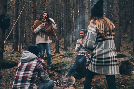 Group of happy young people standing around the campfire while hiking in the woodsの写真素材