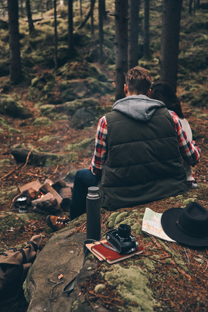Rear view of young couple warming up by the campfire while sitting in the forestの写真素材