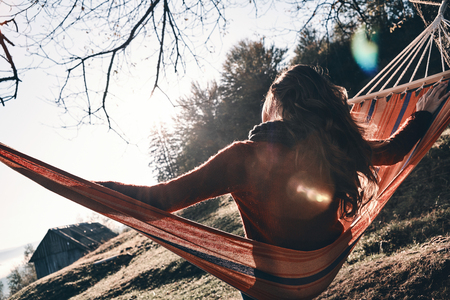 Rear view of young woman keeping arms outstretched while relaxing in hammock outdoorsの写真素材