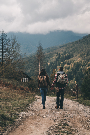 Full length rear view of young couple holding hands while hiking in mountainsの写真素材