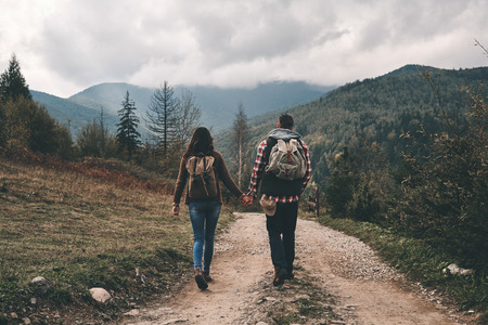 Full length rear view of young couple holding hands while hiking in mountainsの写真素材