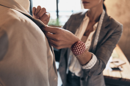 Every detail must be perfect. Close up of young woman adjusting a collar of the jacket on mannequin while standing in her workshopの写真素材